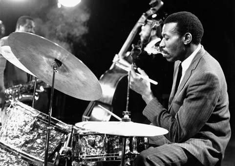 Jazztrummis spelar med cymbal och kontrabasist i bakgrunden